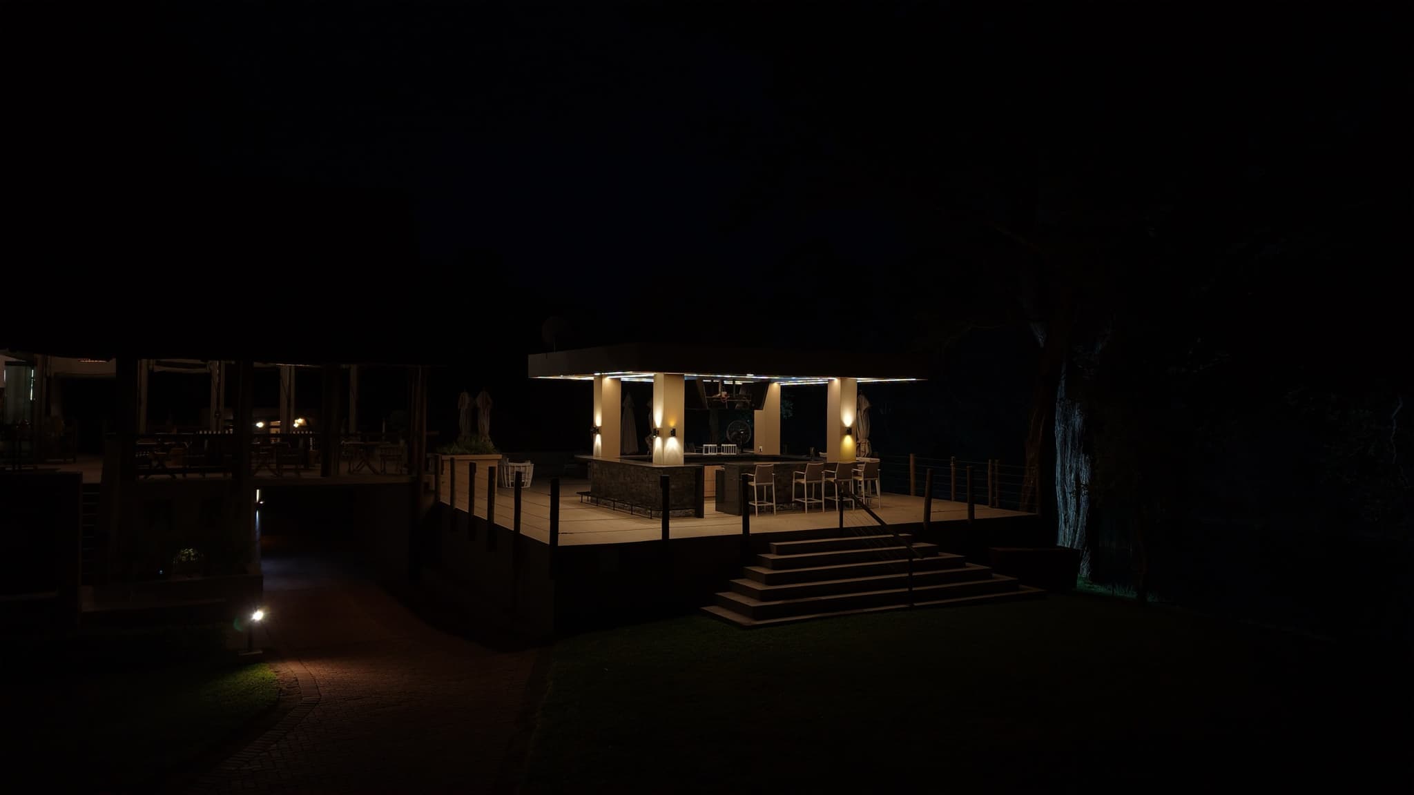 Bar deck lit up at night under ancient trees